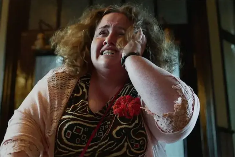 A brown-haired middle aged woman holding her face while visibly in distress
