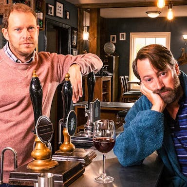 Two middle aged white men looking glum at a pub bar