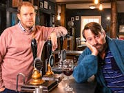 Two middle aged white men looking glum at a pub bar
