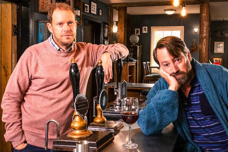 Two middle aged white men looking glum at a pub bar