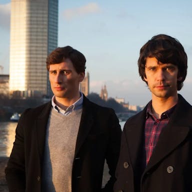 Two young man stand outside against a city backdrop