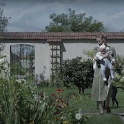 A white woman carrying a baby walking in a large, bright enclosed garden