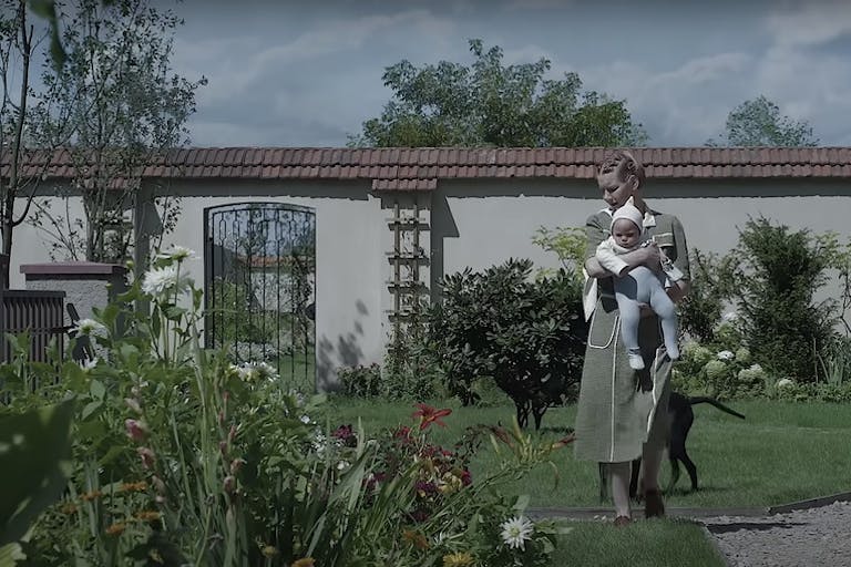 A white woman carrying a baby walking in a large, bright enclosed garden