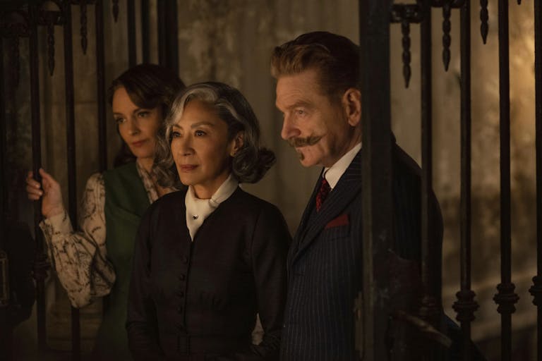 Two women and one man stand in a dark, haunting room