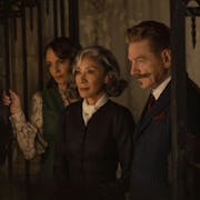 Two women and one man stand in a dark, haunting room