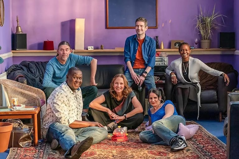 A group of people sitting on the floor and on chairs in a living room