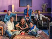 A group of people sitting on the floor and on chairs in a living room