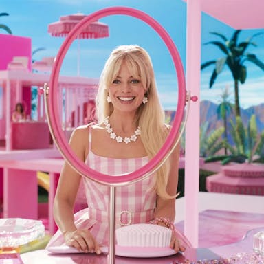A blonde woman smiling widely, looking through an oval frame with missing mirror in a Barbie pink environment 