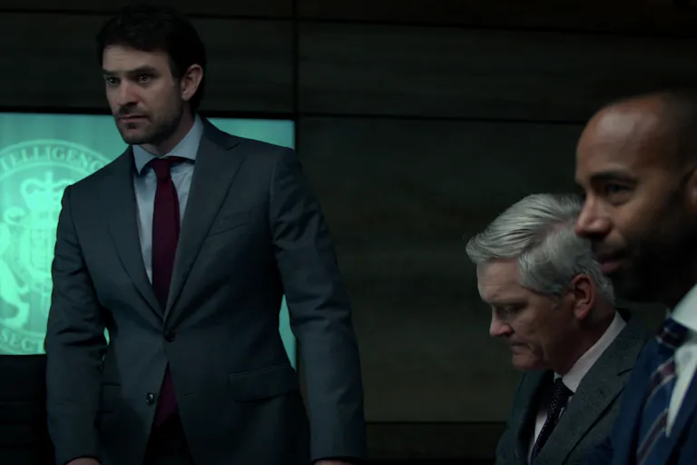 Three men in suits against the backdrop of the MI6 logo on a screen.