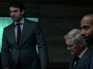 Three men in suits against the backdrop of the MI6 logo on a screen.