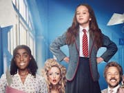 Young girl in school uniform, a red tie and grey blazer, stands with her hands on her hips looking defiantly at the camera, surrounded by other people.