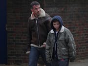 A white man with a wound on his head with blood dripping down walking with a young white boy
