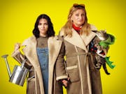 Taller blonde woman and shorter woman with dark hair holding hands, wearing matching sheepskin jackets