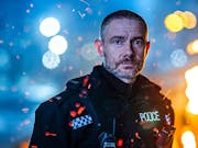Man in British police uniform looks at the camera against the backdrop of city lights at night.