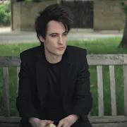 A man and a woman sit on a bench a little distance apart looking sombre