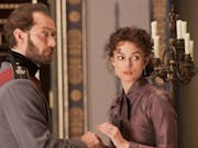A white man in Russian empirical clothing standing with a white woman in aristocratic clothing in a grand house