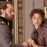 A white man in Russian empirical clothing standing with a white woman in aristocratic clothing in a grand house