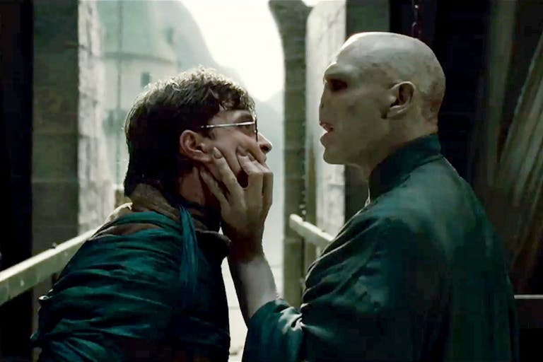 A white man with a snake-like face gripping the face of a young white teen with round glasses