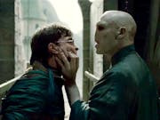 A white man with a snake-like face gripping the face of a young white teen with round glasses