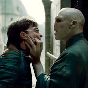 A white man with a snake-like face gripping the face of a young white teen with round glasses