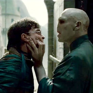 A white man with a snake-like face gripping the face of a young white teen with round glasses 