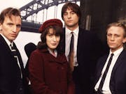 Three white men in suits and a white woman in a red velvet hat and coat