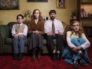 A white family of a Mother, Father, teen daughter and young son, wearing dated, 'respectable' clothing sitting on the sofa and floor