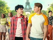 Two male teens holding hands, looking lovingly in each others' eyes, flanked by their friends with the Eiffel Tower in the background