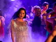 A young white woman in a glamourous silver fringe dress in a purple lit nightclub