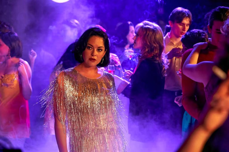 A young white woman in a glamourous silver fringe dress in a purple lit nightclub