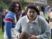A young Maori man in a rugby shirt holding a battered rugby ball looking determined