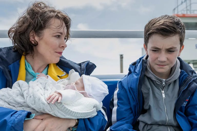 A woman holding a baby sat next to a 12 year old boy on a boat