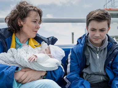 A woman holding a baby sat next to a 12 year old boy on a boat