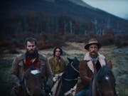 Two white men and a young mixed race man on horseback in a moody rural 1900's setting