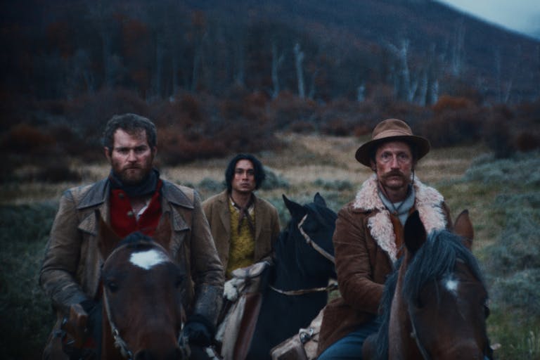 Two white men and a young mixed race man on horseback in a moody rural 1900's setting