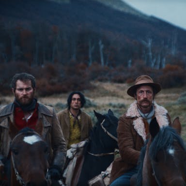Two white men and a young mixed race man on horseback in a moody rural 1900's setting