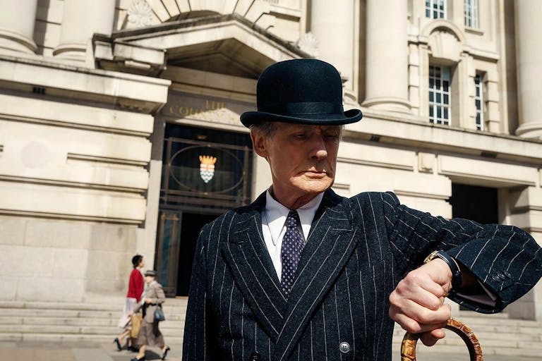 Man in pinstripe suit and bowler hat looks at his watch
