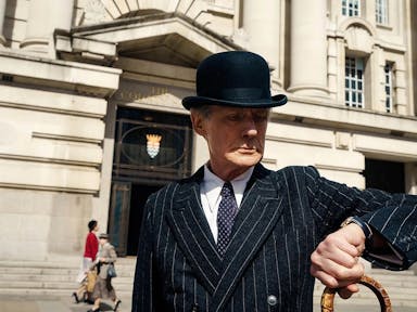 Man in pinstripe suit and bowler hat looks at his watch