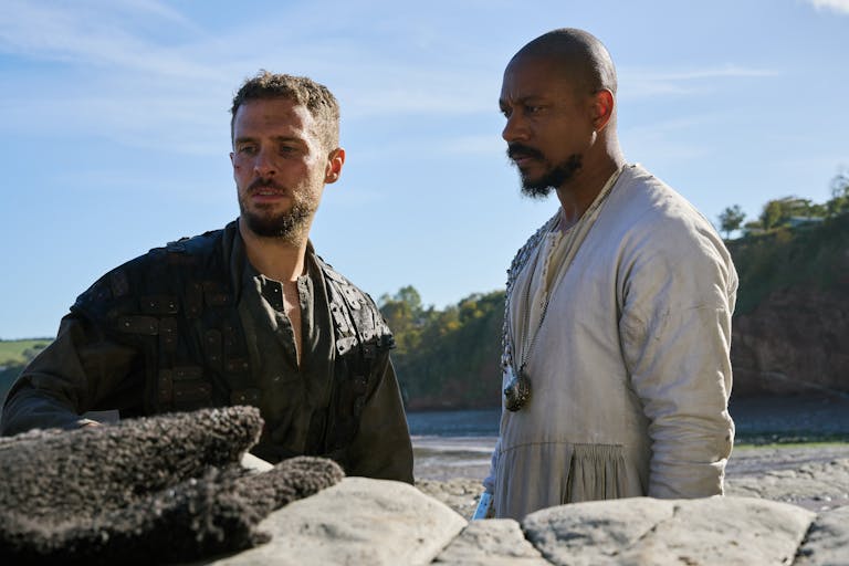 Two men standing beside each other on a beach looking serious
