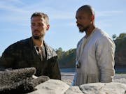 Two men standing beside each other on a beach looking serious