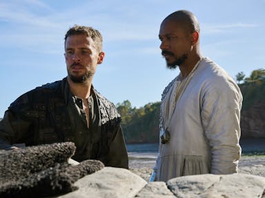 Two men standing beside each other on a beach looking serious