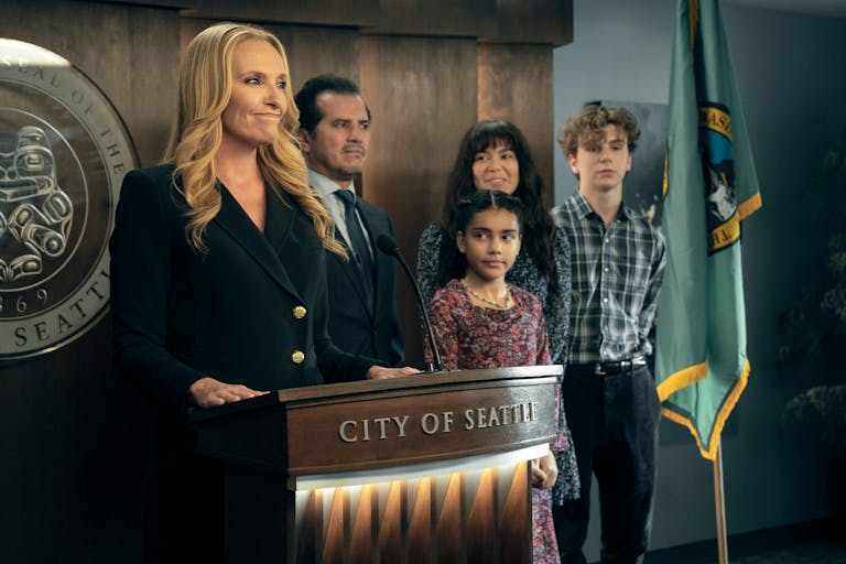 Blonde woman stands at a lectern that reads 'City of Seattle', surrounded by two adults and two children