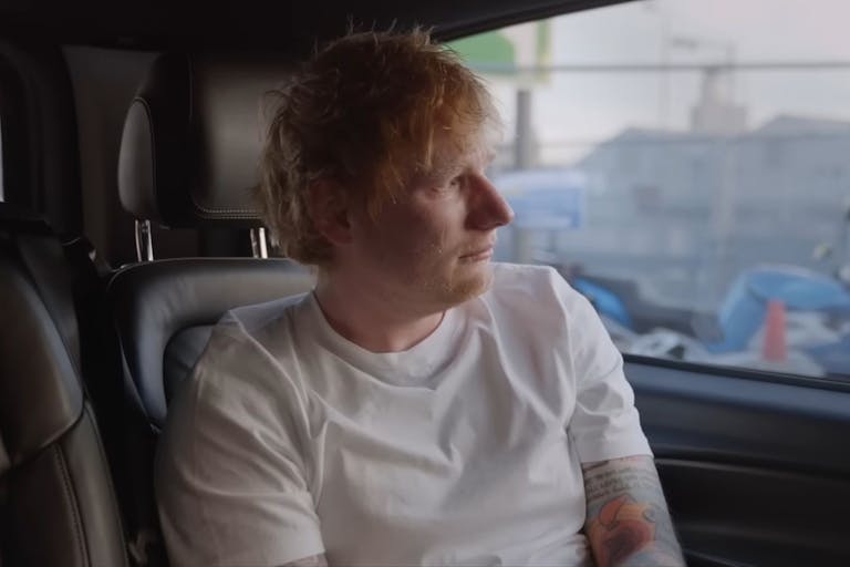 Man in white t-shirt with red hair looks out the window of a car as he is being driven