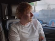Man in white t-shirt with red hair looks out the window of a car as he is being driven