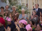 A group of older people wearing celebratory Indian clothing smiling and clapping in the background of a wedding