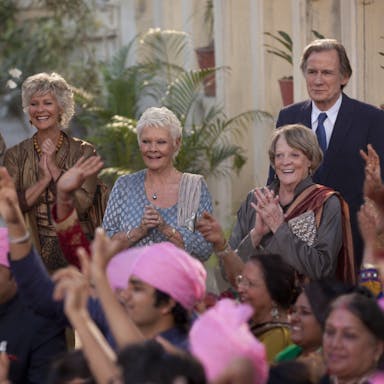 A group of older people wearing celebratory Indian clothing smiling and clapping in the background of a wedding 
