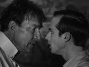 Black and white still of an older white man looking bedraggled and a more put together younger white man facing off