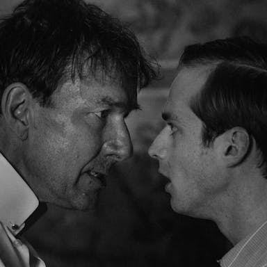 Black and white still of an older white man looking bedraggled and a more put together younger white man facing off