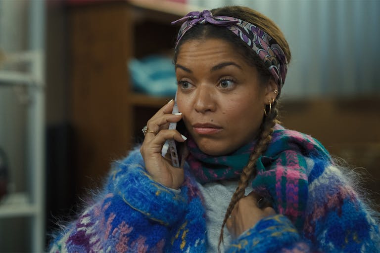 A young Black woman with a mobile phone to her ear, wearing a fluffy multi-coloured jumper