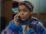 A young Black woman with a mobile phone to her ear, wearing a fluffy multi-coloured jumper